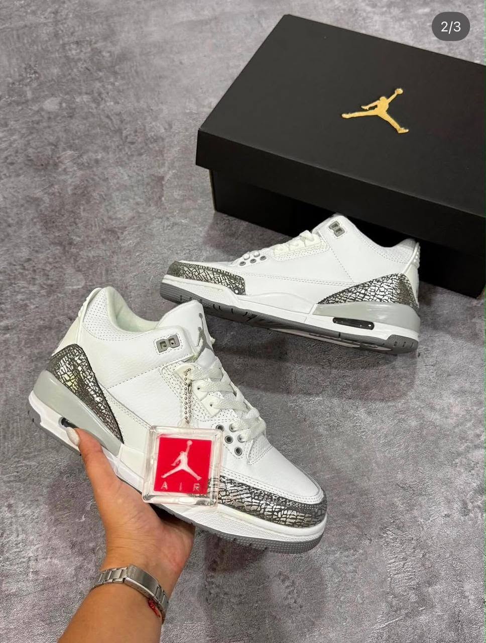 White sneakers held near a black shoe box